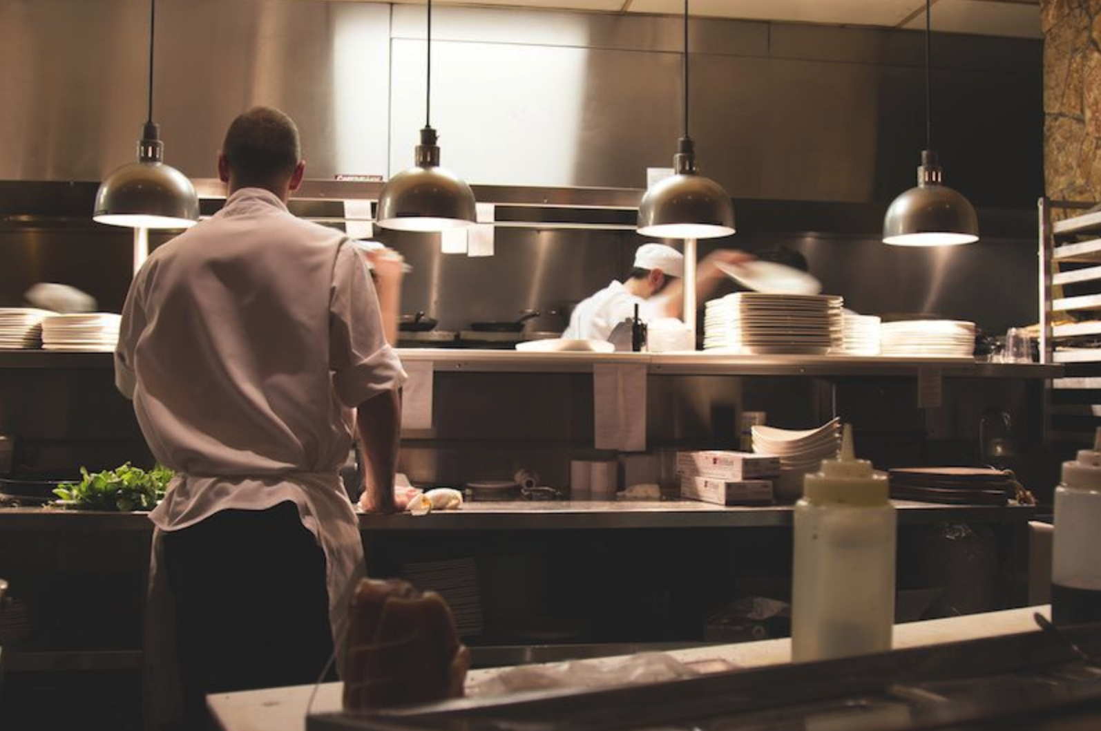 Afbeelding van een restaurantkeuken en een kok die naar bestelbonnetjes kijkt